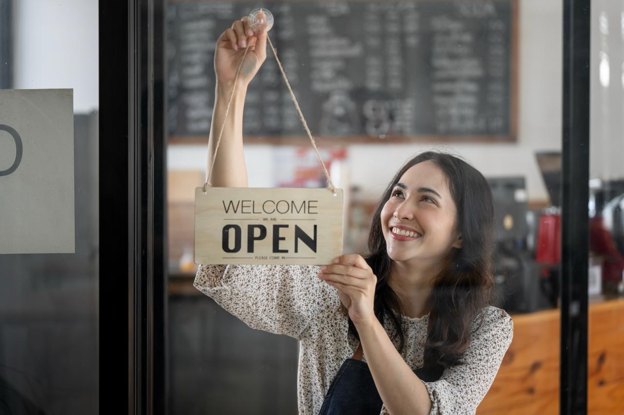A woman hangs an open sign up in a shop window